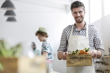 Portrait smiling man holding fresh vegetables in cooking class kitchen - CAIF08762