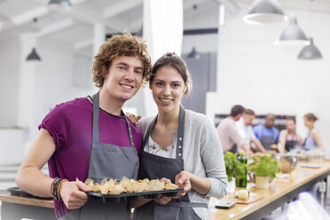 Portrait smiling couple with tray of food in cooking class kitchen - CAIF08779