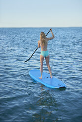 Young woman in bikini paddleboarding in summer ocean - CAIF08783