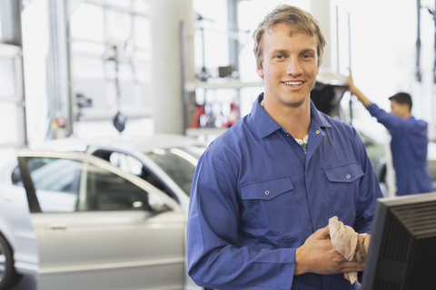 Porträt eines lächelnden Mechanikers am Computer in einer Autowerkstatt, lizenzfreies Stockfoto