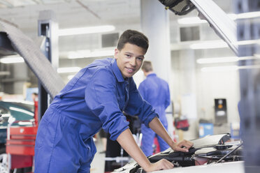 Portrait confident mechanic leaning over car engine in auto repair shop - CAIF08797