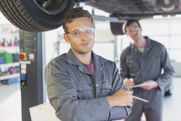 Porträt selbstbewusster Mechaniker unter Auto in Autowerkstatt - CAIF08802