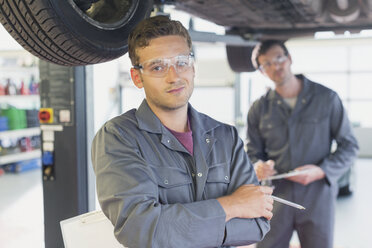 Portrait confident mechanic under car in auto repair shop - CAIF08802