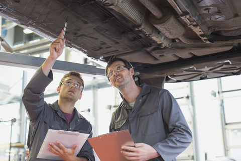 Mechaniker mit Klemmbrettern arbeiten unter dem Auto in einer Autowerkstatt, lizenzfreies Stockfoto