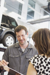 Mechaniker mit Klemmbrett im Gespräch mit einem Kunden in einer Autowerkstatt - CAIF08814