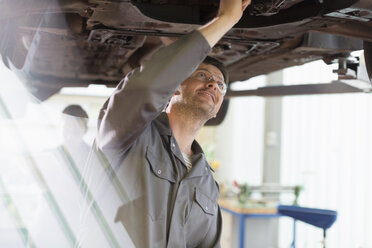 Mechaniker bei der Arbeit unter einem Auto in einer Autowerkstatt - CAIF08825