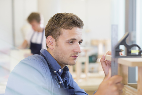 Fokussierter Schreiner misst Holz in der Werkstatt, lizenzfreies Stockfoto