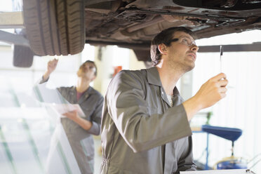 Mechaniker bei der Arbeit unter einem Auto in einer Autowerkstatt - CAIF08827