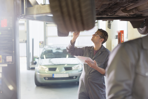 Mechaniker mit Klemmbrett unter dem Auto in der Autowerkstatt, lizenzfreies Stockfoto