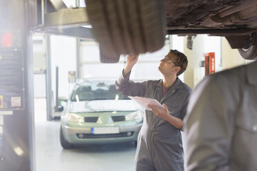 Mechaniker mit Klemmbrett unter dem Auto in der Autowerkstatt - CAIF08829