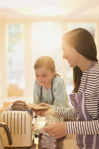 Mutter und Tochter rösten Brot in der Küche, lizenzfreies Stockfoto