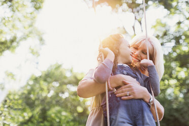 Grandmother hugging granddaughter on swing - CAIF08852