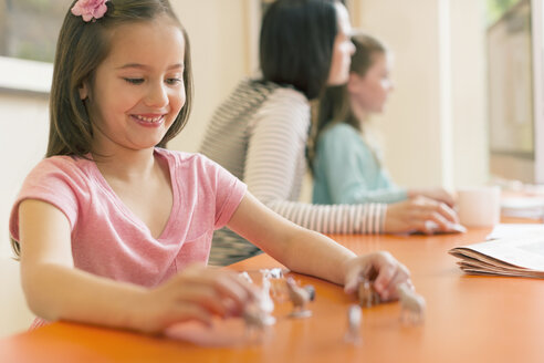 Lächelndes Mädchen spielt mit Miniaturspielzeugtieren - CAIF08854