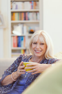 Portrait lächelnde ältere Frau trinkt Kaffee auf Sofa - CAIF08860