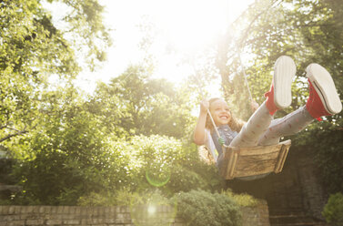 Carefree girl swinging in sunny backyard - CAIF08866