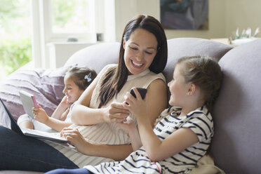 Mother and daughters with cell phone, laptop and digital tablet on sofa - CAIF08868