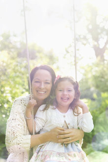 Porträt lächelnde Mutter umarmt Tochter auf Schaukel im Park - CAIF08870