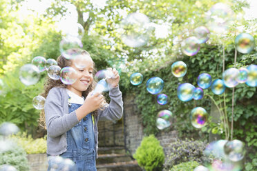 Girl blowing bubbles in backyard - CAIF08880