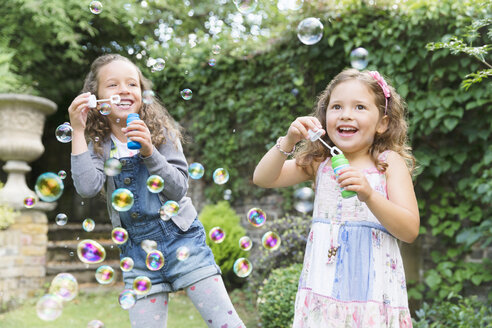 Carefree girls blowing bubbles in backyard - CAIF08882