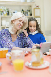 Großmutter und Enkelin benutzen ein digitales Tablet am Frühstückstisch - CAIF08883