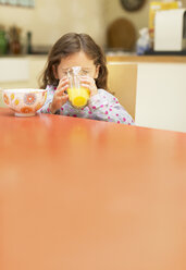 Girl drinking orange juice at breakfast table - CAIF08886