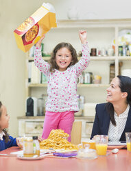 Portrait enthusiastic girl cheering with cereal box at breakfast table - CAIF08889