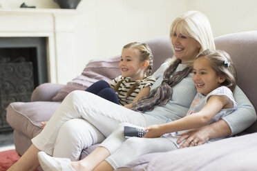 Grandmother and granddaughters watching TV on living room sofa - CAIF08901