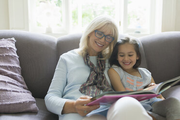 Großmutter und Enkelin lesen ein Buch auf dem Wohnzimmersofa - CAIF08903