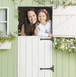 Porträt lächelnde Mutter und Tochter im Fenster des Spielhauses - CAIF08904