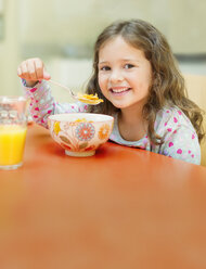 Portrait smiling girl eating cereal at breakfast table - CAIF08909