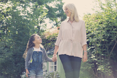 Grandmother and granddaughter holding hands and walking in garden - CAIF08917