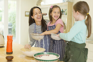 Lachende Mutter und Töchter beim Backen mit Mehl im Gesicht in der Küche - CAIF08924