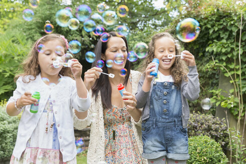 Mother and daughters blowing bubbles in backyard - CAIF08930