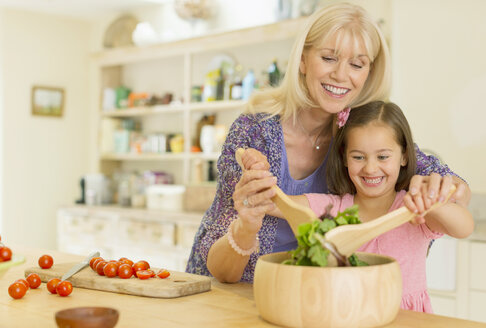 Großmutter und Enkelin beim Salatschwenken in der Küche - CAIF08938