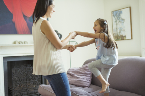 Verspielte Mutter und Tochter tanzen im Wohnzimmer, lizenzfreies Stockfoto