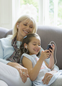 Großmutter und Enkelin teilen sich Kopfhörer und hören Musik auf dem Sofa - CAIF08941