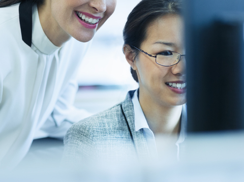 Lächelnde Geschäftsfrauen arbeiten am Computer im Büro, lizenzfreies Stockfoto