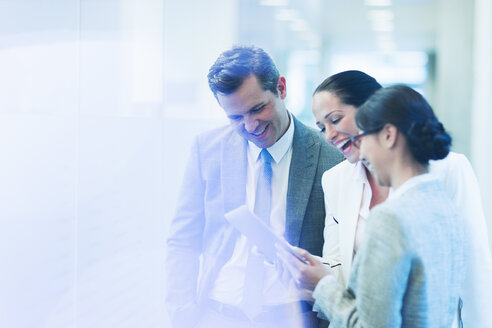 Business people with digital tablet laughing in office corridor - CAIF08961