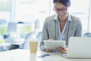 Lächelnde Geschäftsfrau mit digitalem Tablet und Kaffee im Büro - CAIF08990