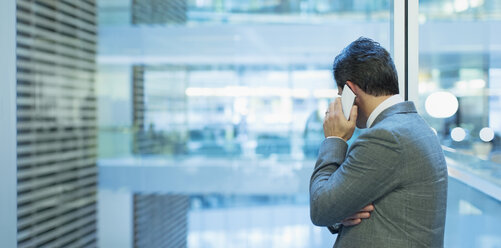 Businessman talking on cell phone at office window - CAIF09001