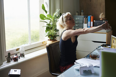 Junge Frau streckt die Arme am Schreibtisch im Home Office - CAIF09010