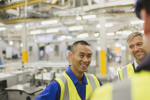 Arbeiter in reflektierender Kleidung im Gespräch in einer Fabrik, lizenzfreies Stockfoto