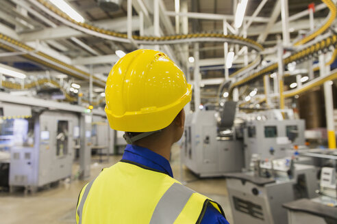 Arbeiter im Schutzhelm, der die Förderbänder und Maschinen der Druckmaschine in der Druckerei beobachtet - CAIF09034