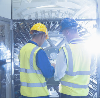 Arbeiter mit Klemmbrett bei der Kontrolle von Maschinen in einer Druckerei - CAIF09038