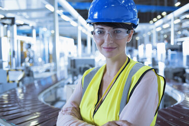 Porträt einer selbstbewussten Arbeiterin mit Schutzhelm und Schutzbrille in einer Fabrik - CAIF09060