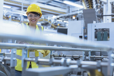 Porträt einer lächelnden Arbeiterin an einer Maschine in einer Fabrik - CAIF09067