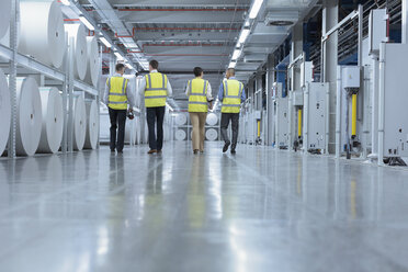 Arbeiter in reflektierender Kleidung gehen an großen Papierrollen in einer Druckerei vorbei - CAIF09071