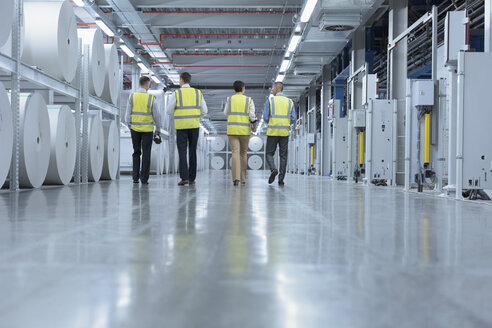 Workers in reflective clothing walking past large paper spools in printing plant - CAIF09071