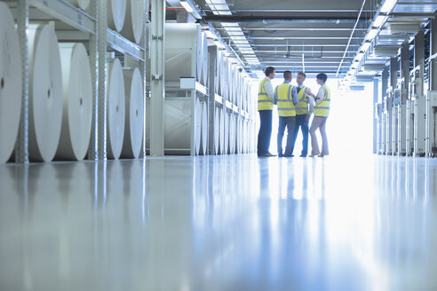 Arbeiter unterhalten sich in der Nähe großer Papierspulen in einer Druckerei - CAIF09075