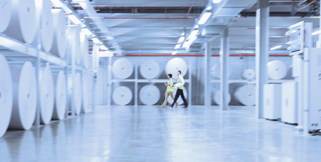 Arbeiter gehen entlang großer Papierrollen in einer Druckerei - CAIF09080
